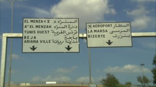Zwei Straßenschilder. Auf der linken Hälfte sind die Orte auf Französisch ausgeschildert, rechts auf Arabisch. 