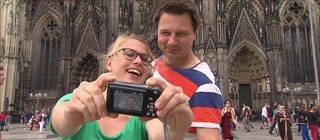 Eine Frau und ein Mann machen ein Selfie vor dem Kölner Dom.