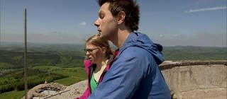 Ein Mann und eine Frau stehen auf einer Aussichtsplattform und schauen ins Tal hinab.
