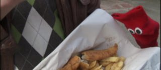 Eine Hand hält eine Portion Fish and Chips.