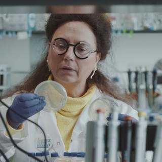 Eine Frau im Laborkittel betrachtet eine Petrischale in ihrer Hand.