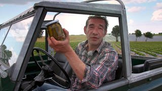 Ein Mann in einem Auto hält ein Glas eingelegte Gurken in der Hand.