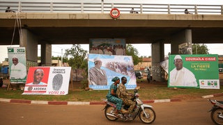 Wahlkampf in Mali für die Präsidentschaftswahl 2018 – ein junges Paar fährt auf einem Moped an Wahlplakaten vorbei